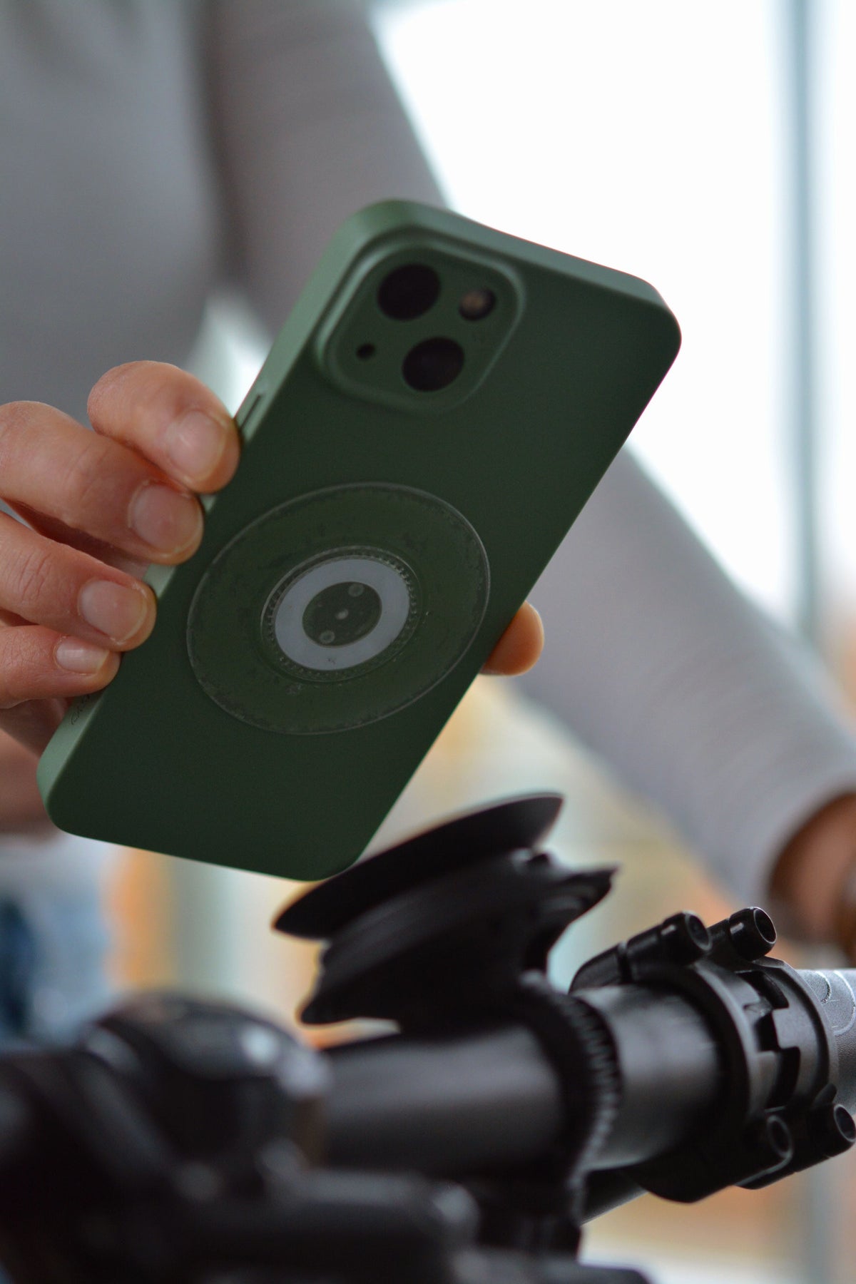 Adesivo universale FIDLOCK VACUUM per smartphone trasparente — adesivo trasparente applicato al telefono, mostrato davanti a un supporto VACUUM